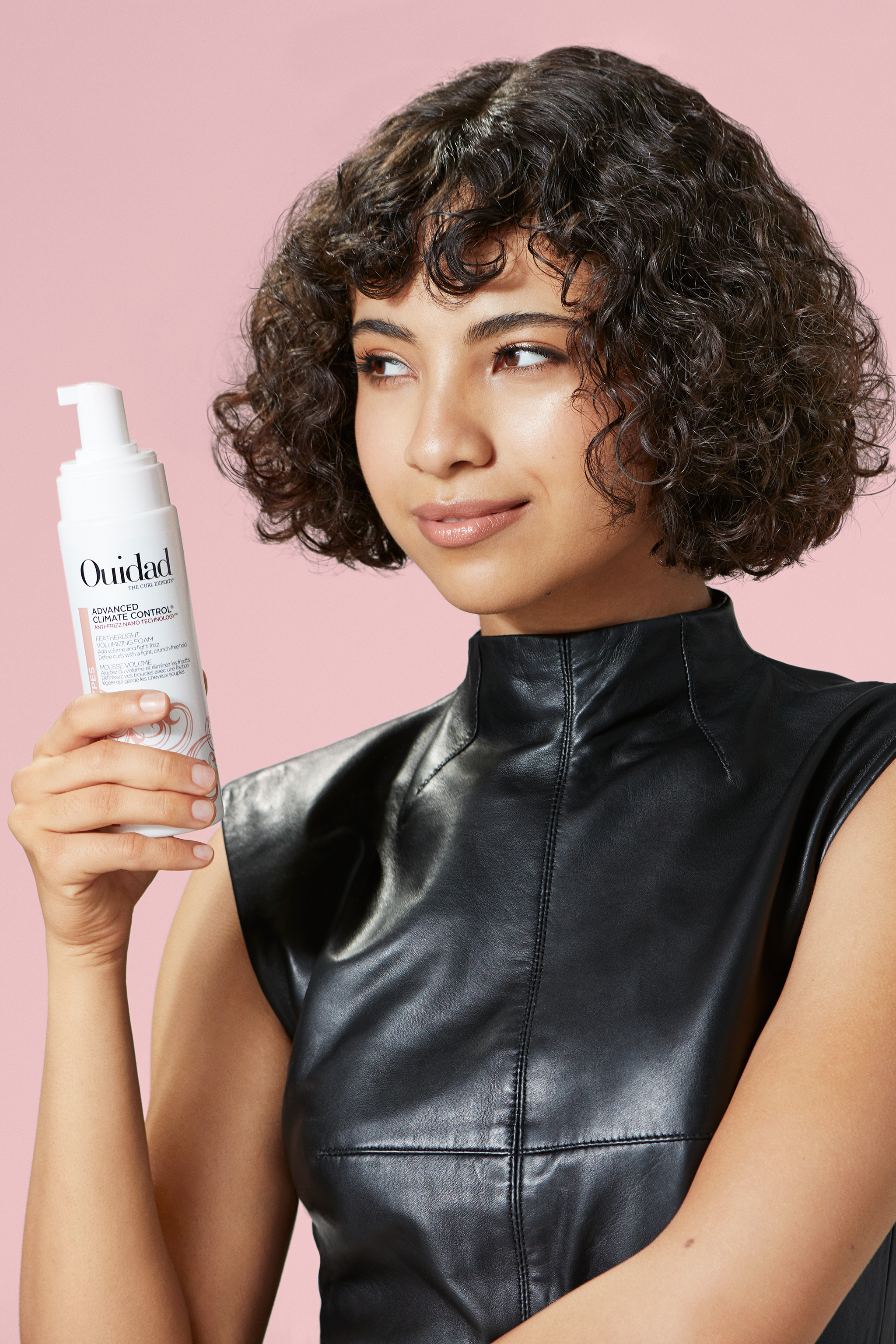 Woman with curly hair looking off to the side while holding a bottle of Ouidad Advanced Climate Control.